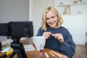 porträtt av ung leende kvinna i henne rum, inspelning på kamera, livsstil vlog för social media, innehav mascara, granskning henne smink skönhet Produkter, som visar på vilket sätt till använda sig av kosmetika foto