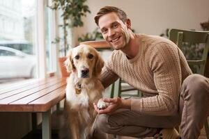 porträtt av en härlig gyllene retriever och stilig man i Kafé. söt hund ger Tass och tar bild med hans ägare i kaffe affär foto