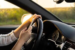 kvinna sändning meddelanden med smartphone medan körning bil. kvinna förare använder sig av mobil telefon på de väg under körning de bil. säkerhet och teknologi begrepp foto