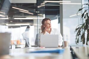 koncentrerad mogna skön affärskvinna arbetssätt på bärbar dator i ljus modern kontor foto