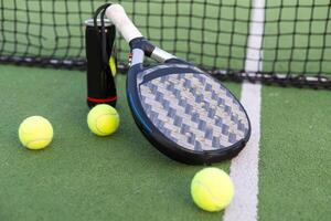 gul bollar på gräs torva nära padel tennis racket Bakom netto i grön domstol utomhus med naturlig belysning. paddla är en racketen spel. professionell sport begrepp med kopia Plats. foto