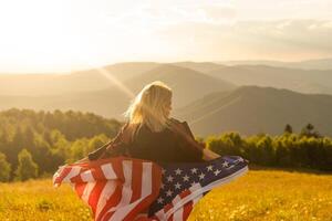 ung Lycklig flicka löpning och Hoppar sorglös med öppen vapen över vete fält. innehav USA flagga foto