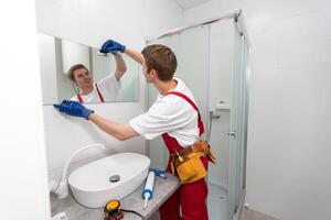 manlig reparatör hänger de modern elektronisk badrum spegel. Tillbehör och möbel för badrum och hus foto