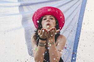 Söt kvinna med färgrik sugrör hatt blåser konfetti foto