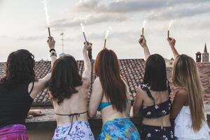 grupp av Lycklig kvinna vänner innehav sparklers på taket fest foto