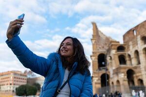 Lycklig mitten åldrig kvinna på semester tar en selfie i främre av coliseum amfiteater i rom foto