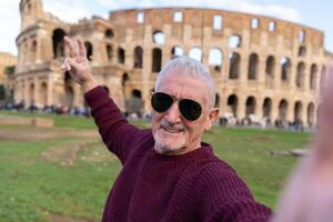 Lycklig mitten åldrig man på semester tar en selfie i främre av coliseum amfiteater i rom foto