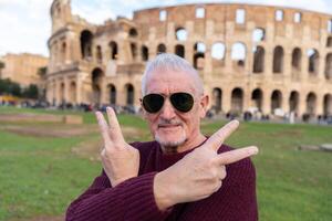 Lycklig mitten åldrig man på semester tar en selfie i främre av coliseum amfiteater i rom foto