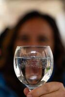 suddigt mitten åldrig kvinna på utomhus- restaurang som visar henne reflexion i en glas av vatten foto