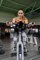 ung söt kvinna i tajt sporter kostym Träning på övning cykel i Gym foto