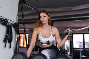 ung charmig blond kvinna i sportkläder lyft hantlar i en Gym foto