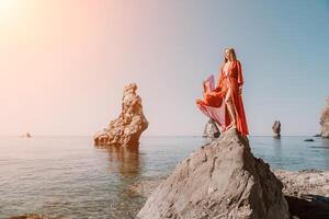 kvinna resa hav. ung Lycklig kvinna i en lång röd klänning Framställ på en strand nära de hav på bakgrund av vulkanisk stenar, tycka om i Island, delning resa äventyr resa foto