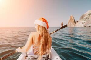kvinna i kajak tillbaka se. Lycklig ung kvinna i santa hatt flytande i kajak på lugna hav. sommar Semester semester och glad kvinna människor avkopplande har roligt på de båt. foto
