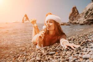 kvinna resa hav. Lycklig turist njut av tar bild på de strand för minnen. kvinna resande i santa hatt utseende på kamera på de hav bukt, delning resa äventyr resa foto