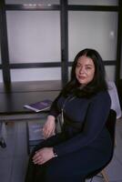 porträtt av en medium storlek kvinna med svart hår i en svart klänning i ett kontor foto