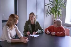 tre kvinnor, Inklusive en person med en handikapp, diskutera de företagets strategi på en möte i de kontor foto