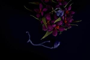 ametist ringa och en hängsmycke av papper blommor i en blå vas på en svart bakgrund foto