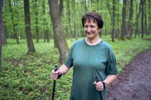 äldre kvinna är engagerad i nordic gående med pinnar i de vår skog foto