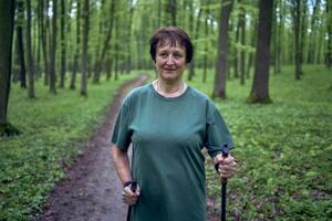 äldre kvinna är engagerad i nordic gående med pinnar i de vår skog foto