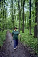 äldre kvinna är engagerad i nordic gående med pinnar i de vår skog foto