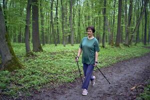 äldre kvinna är engagerad i nordic gående med pinnar i de vår skog foto