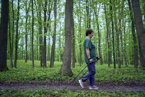 äldre kvinna är engagerad i nordic gående med pinnar i de vår skog foto