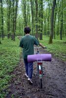 äldre kvinna gående i vår skog med cykel och yoga matta foto