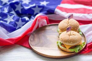 närbild av hemlagad två hamburgare med sallad och ost har ett amerikan flagga stift på de hamburgare placerad på en trä- hackning styrelse med ett amerikan flagga bakgrund på en trä- tabell foto
