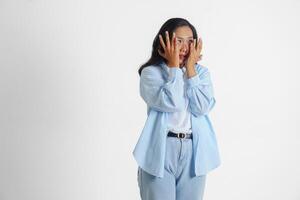 asiatisk kvinna bär tillfällig blå skjorta är gestikulerar skrämd gest med händer och beläggning henne ansikte, isolerat vit bakgrund foto