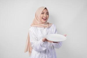 skön ung asiatisk muslim kvinna i hijab presenter ett tömma tallrik med kopia Plats över Det, som visar de mat meny för iftar foto