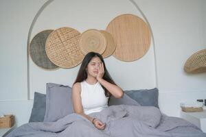 asiatisk kvinna vakna upp i de morgon- känsla betonade och få huvudvärk efter djup sova, fortfarande känsla trött och sömnig stanna kvar Sammanträde på säng i de sovrum foto