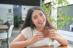 ung asiatisk kvinna innehav och som visar en svart tallrik av munk bakverk som heter cromboloni med choklad fyllning för mellanmål tid, leende med en Lycklig och glad uttryck foto