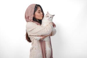 attraktiv ung asiatisk muslim kvinna i slöja hijab leende medan Framställ och kramas en vit ragdoll katt sällskapsdjur foto