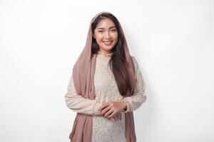 porträtt av skön asiatisk muslim kvinna bär slöja hijab ger med formell utgör leende till de kamera, stående över isolerat vit bakgrund foto