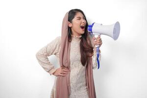 livlig ung asiatisk muslim kvinna bär slöja slöja hijab skrikande på megafon, isolerat på vit bakgrund studio. ramadan och eid mubarak begrepp. foto