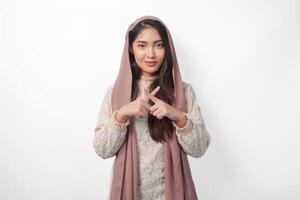 ung asiatisk muslim kvinna bär slöja hijab gestikulerar en Nej avslag, vägra använder sig av händer och fingrar, isolerat förbi vit bakgrund. ramadan och eid mubarak begrepp foto
