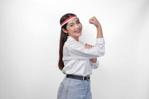 ung asiatisk kvinna full av förtroende höjning en näve upp hand tecken gest, bär flagga pannband och vit skjorta, visning en stark flicka utgör. oberoende dag begrepp foto