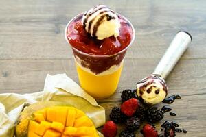 gyllene smoothie av mango, jordgubb och mullbär med is grädde skopa eras i disponibel glas isolerat på tabell sida se av friska morgon- smoothie dryck foto