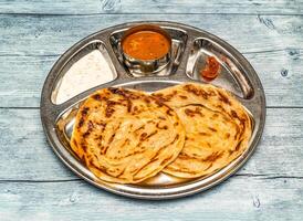 roti prata, paratha, parata, poratha med curry, raita och ättikslag eras i thali maträtt isolerat på trä- tabell topp se av indisk kryddad mat foto