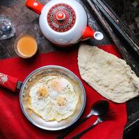 friterad ägg med bröd, kaffe och tekanna eras i maträtt isolerat på röd matta topp se på tabell arabicum mat foto