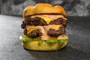 kryddad dubbel- nötkött burger inkludera tomat, sallad blad, smält ost och majonnäs isolerat på mörk grå bakgrund sida se av snabb mat smörgås foto