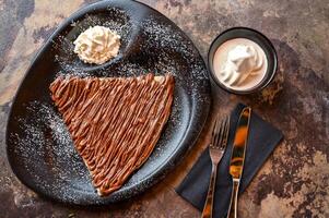 nutella crepe varm choklad med vispad grädde, kniv och gaffel eras i maträtt isolerat på mörk bakgrund närbild topp se av Kafé bakad efterrätt mat foto