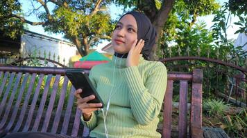 Lycklig muslim kvinna lyssna musik på mobil telefon på parkera, använder sig av headset, fri Plats foto