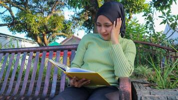 avslappnad muslim kvinna njuter helgen på parkera, Sammanträde på bänk och läsning bok, tömma Plats foto