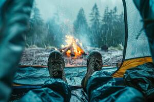 ai genererad Foto av en se från inuti en tält med en personens fötter, ser ut på en lägereld under en regnig himmel
