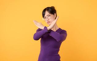 utforska begrepp av avslag och avslag genom x gest tillverkad allvarlig ung kvinna bär lila skjorta och glasögon i studio porträtt mot en gul bakgrund. ett effektfull symbol för varning. foto