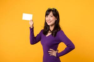 mot en vibrerande gul bakgrund, en modern kvinna, i lila skjorta och solglasögon, ställer ut ett tömma kort, en tom skiffer för din meddelande. foto