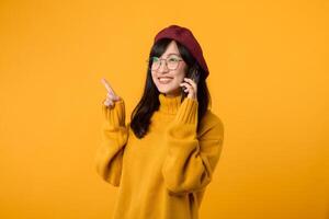 porträtt ung Söt asiatisk kvinna 30s bär gul Tröja och röd basker känsla Lycklig medan använder sig av smartphone utforska de värld. mobil Ansökan begrepp. foto