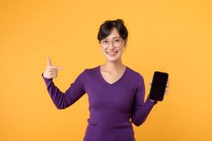 utforska de värld av teknologi med en glad ung kvinna, bär en lila skjorta och glasögon, använder sig av henne smartphone för social Framgång och glad uppkopplad handla mot en gul bakgrund foto