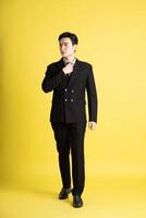 porträtt av asiatisk manlig affärsman. bär en kostym och Framställ på en gul bakgrund foto